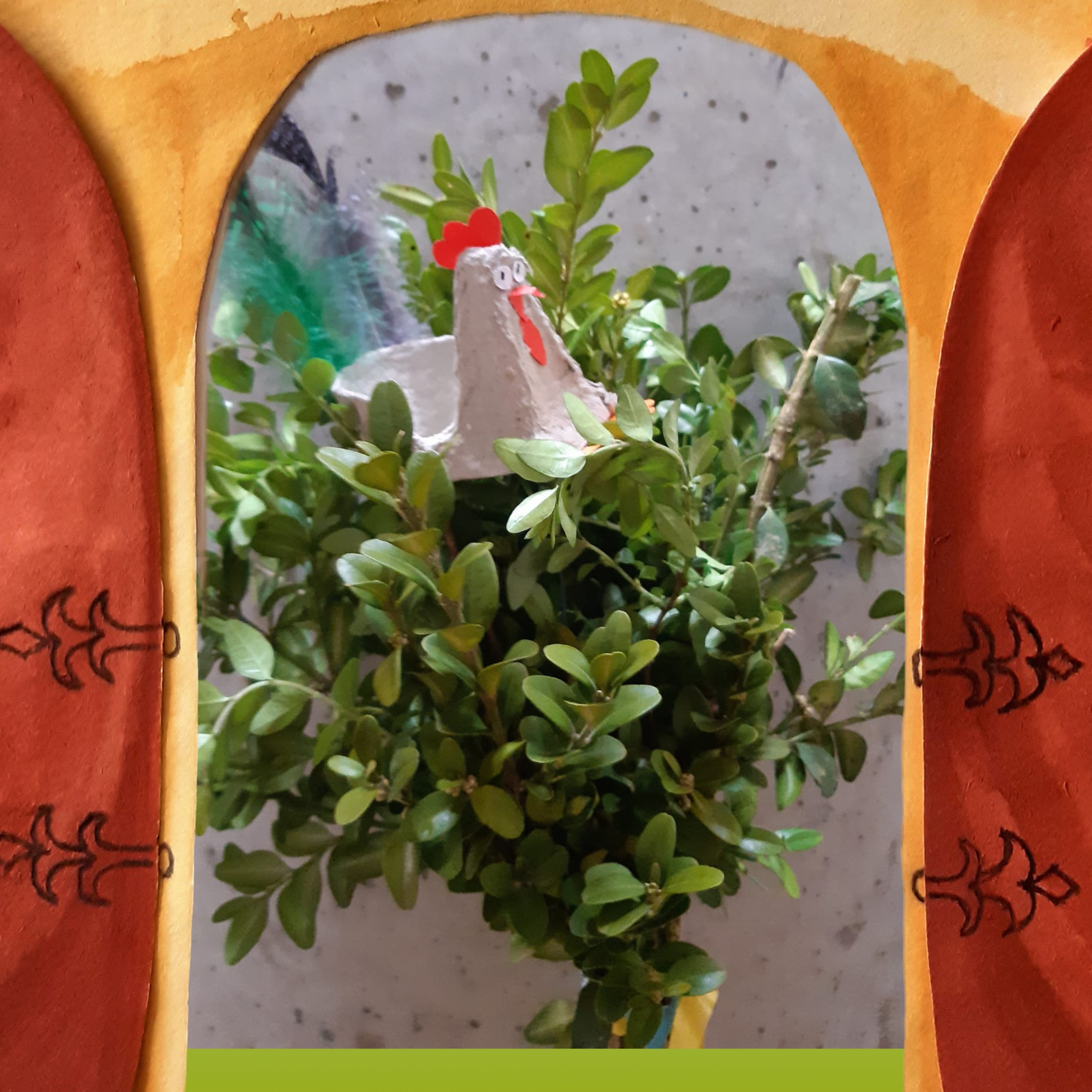 Hinter einem Torbogen kommt ein Palmbusch zum Vorschein, der einen Hahn aus Eierkarton in sich trägt.