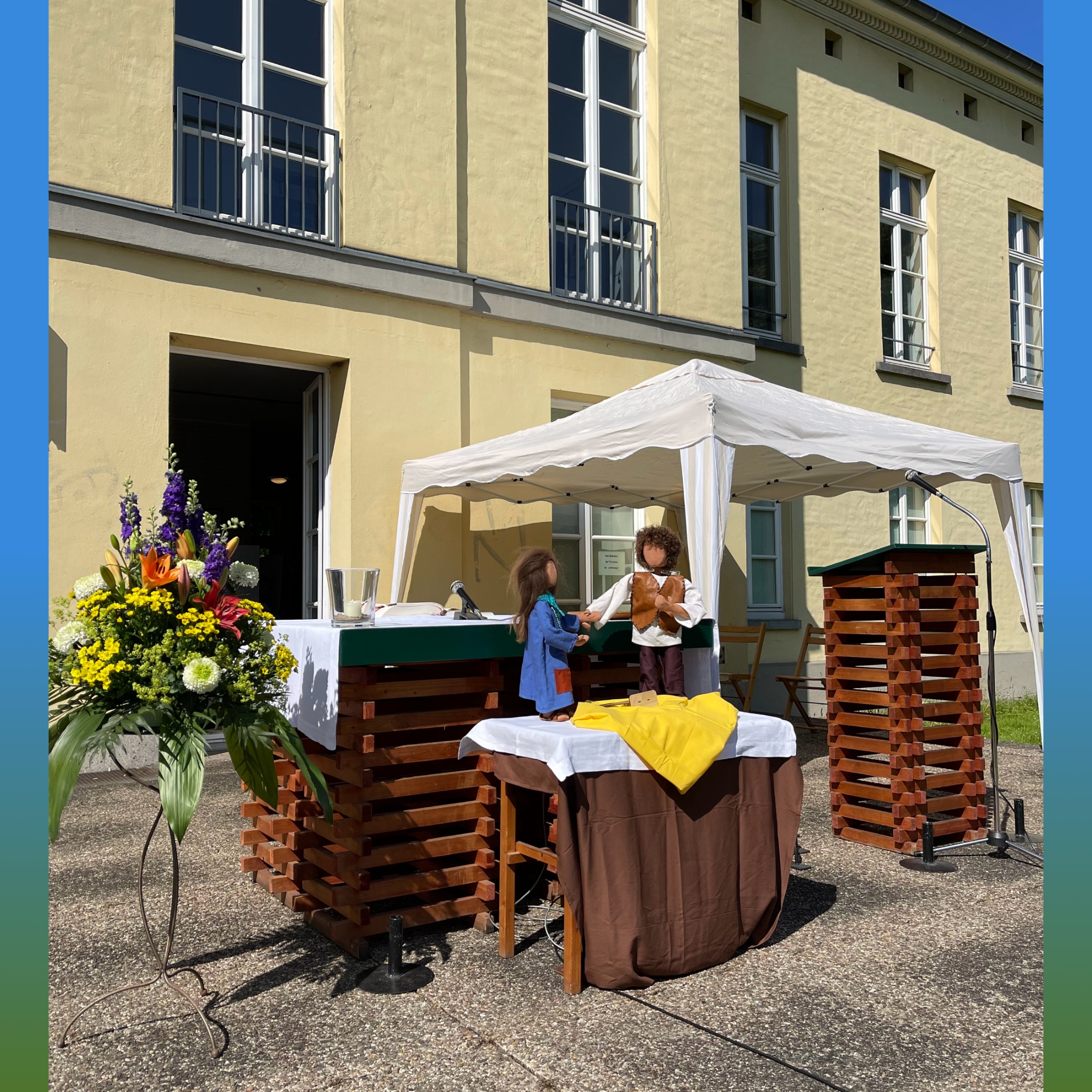 Altar und Ambo aus Pax Christi stehen im Freien vor einem Haus, daneben ein Strauß mit gesteckten Blumen, im Hintergrund ein Pavillon, der Schatten für die Sitzenden spendet