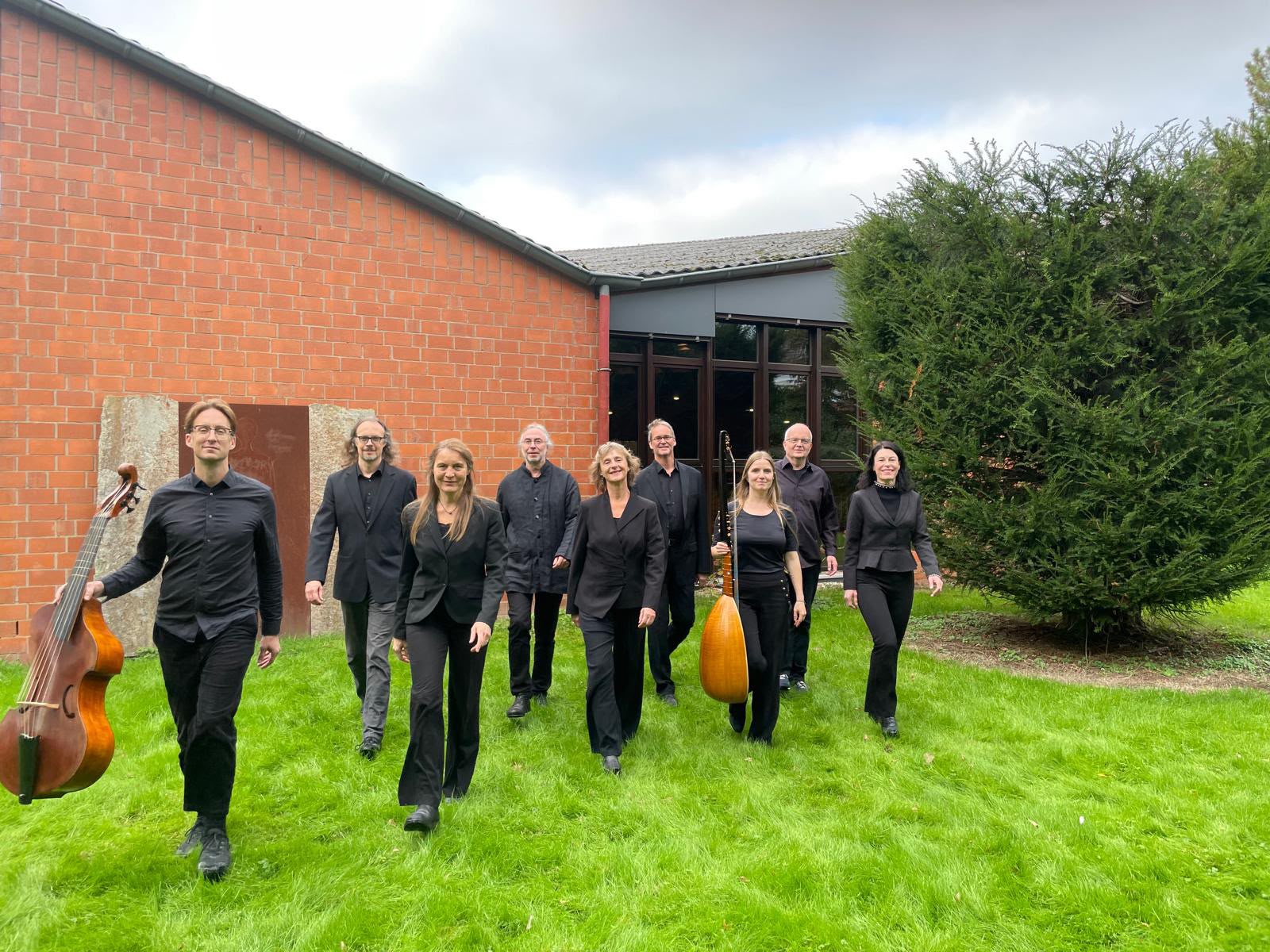 Mehrere Personen in schwarzer Kleidung laufen auf den Fotografen zu, einige von ihnen tragen Musikinstrumente bei sich. Im Hintergrund Pax Christi.