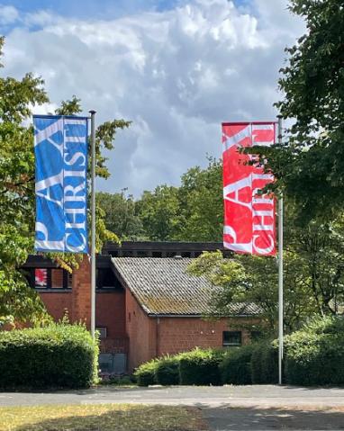 Blick auf Außenansicht Pax Christi mit roter und blauer Fahne