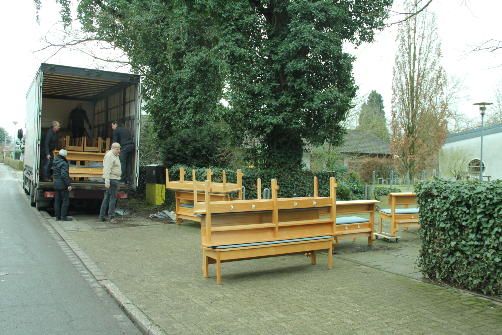 Vor dem grünen Baum stehen die Kirchenbänke. Im LKW sind bereits einige Bänke eingeladen.