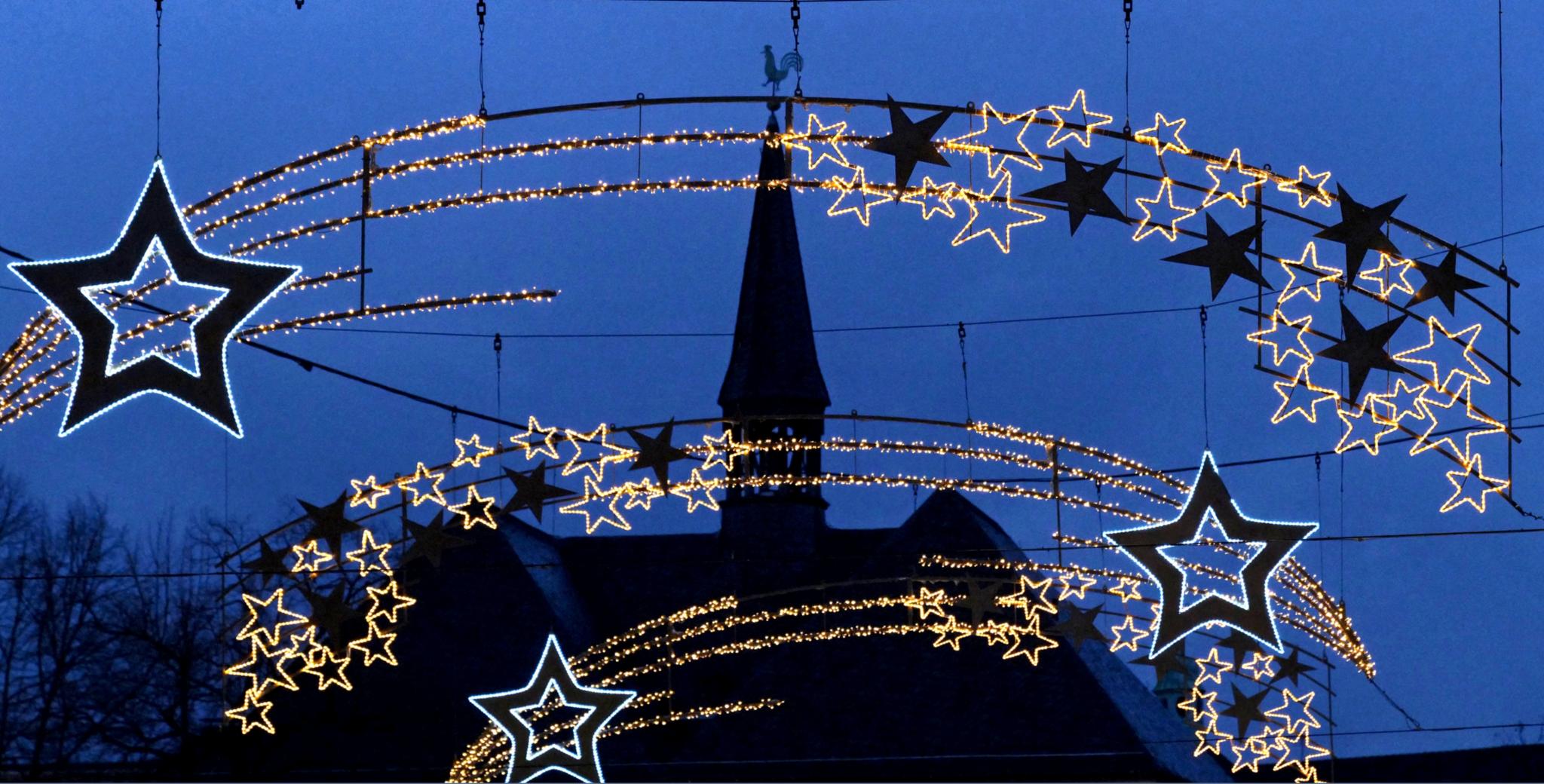 kirche_weihnachtsbeleuchtung_Sterne_blau Weihnachtsbeleuchtung mit Sternmotiven vor Kirchturm bei Dämmerung.