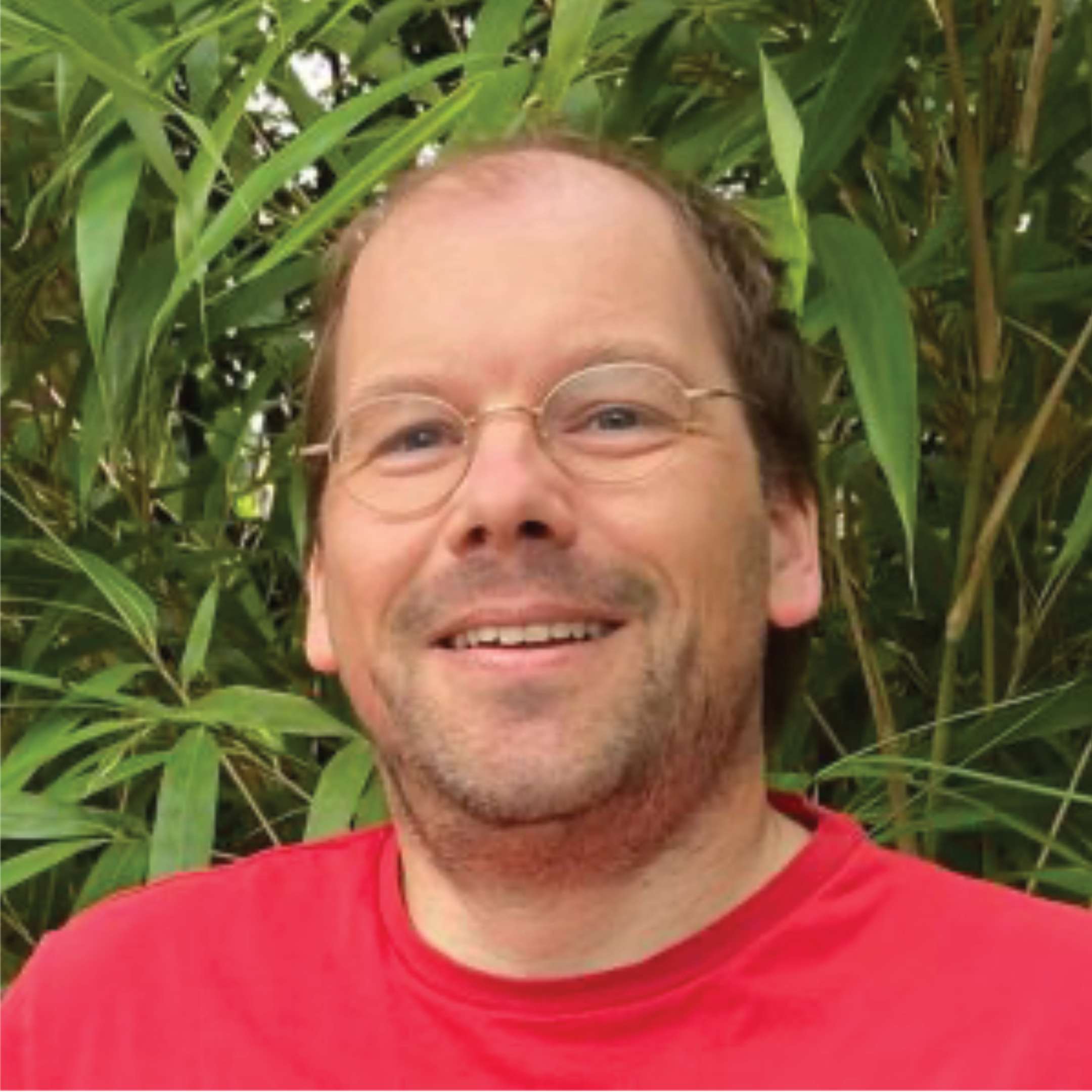Ein Mann in einem roten Shirt steht vor grünen Pflanzen.