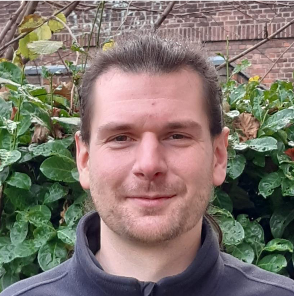 Ein junger Mann  vor einer grünen Hecke.