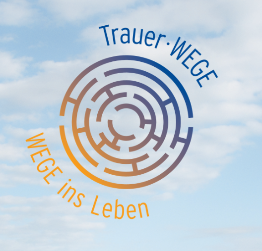 Kreisförmiges Labyrinth mit dem Schriftzug 'Trauer·WEGE' oben und 'WEGE ins Leben' unten vor wolkigem Himmel.