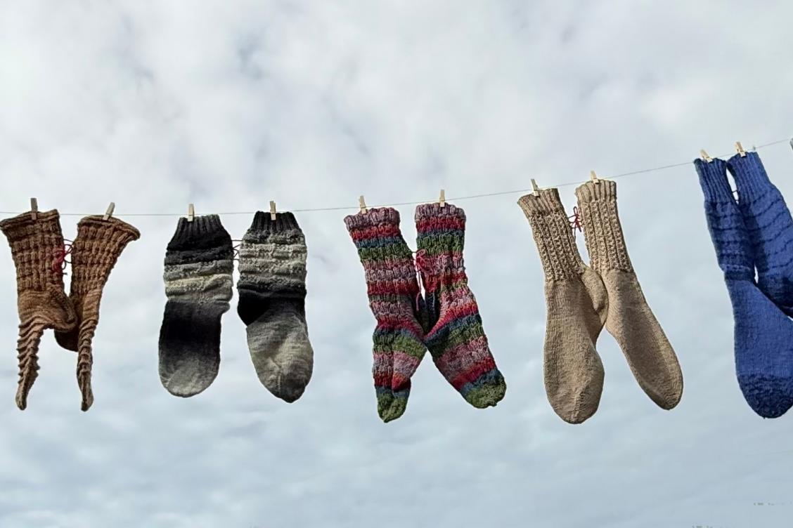 Mehrere bunte gestrickte Socken hängen an einer Wäscheleine vor bewölktem Himmel.