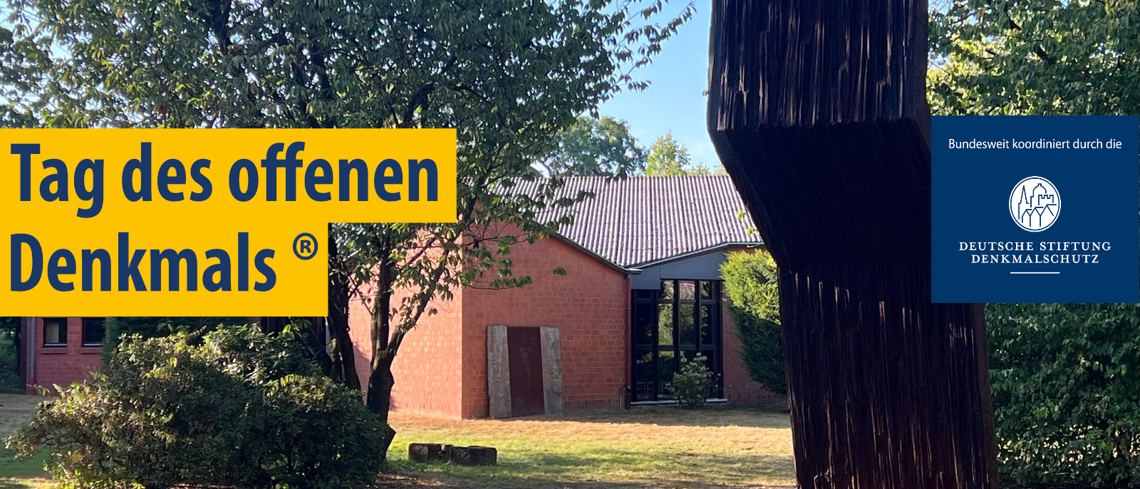 Skulptur aus dunklem Material vor einem roten Backsteingebäude mit Bäumen und gelbem Schriftzug 'Tag des offenen Denkmals (R)' sowie blauem Einstecker mit 'bundesweit koordiniert durch die Deutsche Stiftung Denkmalschutz'.