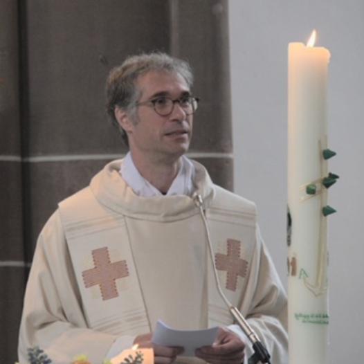 Pfr. Bühner neben der Osterkerze stehend schaut in den Raum.