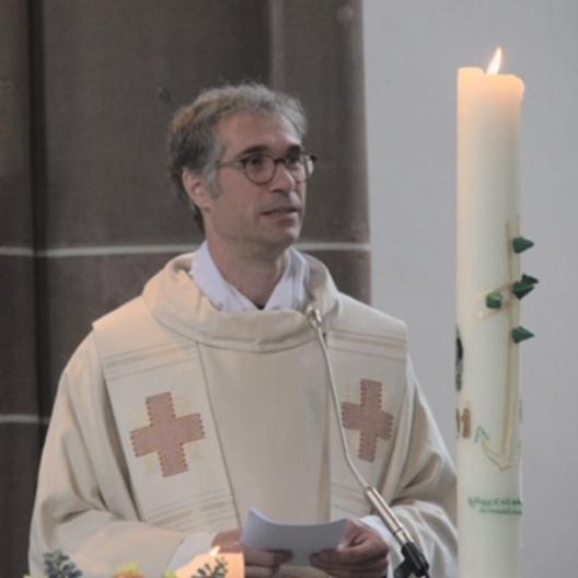 Pfr. Bühner neben der Osterkerze stehend schaut in den Raum.