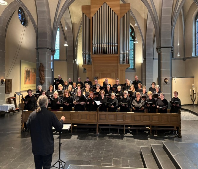 Chormitglieder stehen singend vor der St. Clemens-Orgel und singen gemeinsam. Im Vordergrund steht der Dirigent.