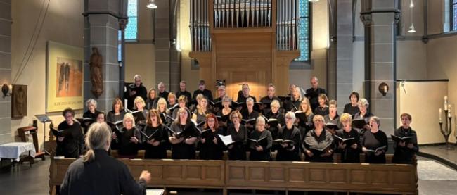 Chormitglieder stehen singend vor der St. Clemens-Orgel und singen gemeinsam. Im Vordergrund steht der Dirigent.
