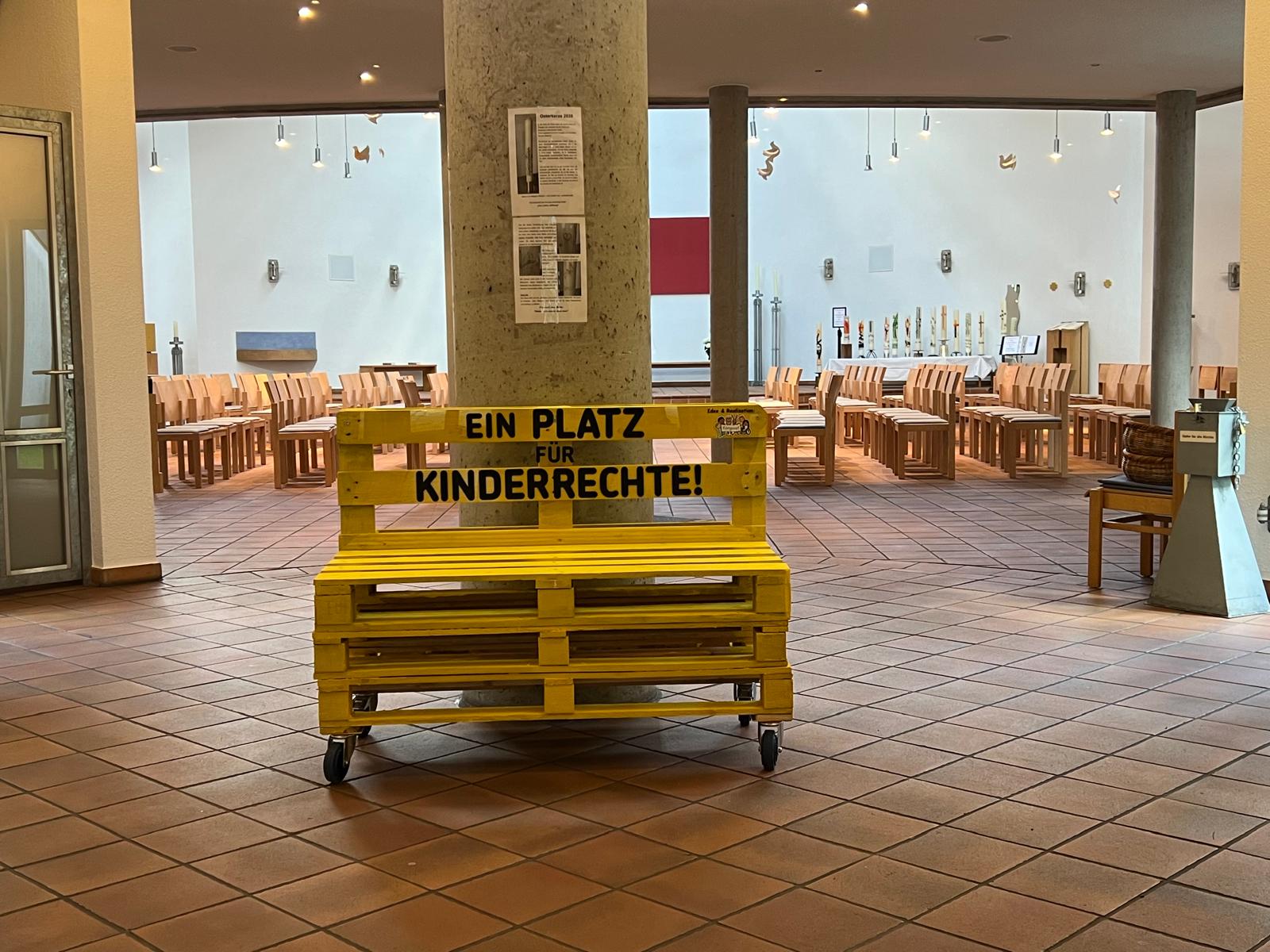 Ein gelbes Palettensofa steht vor einer grauen Säule.