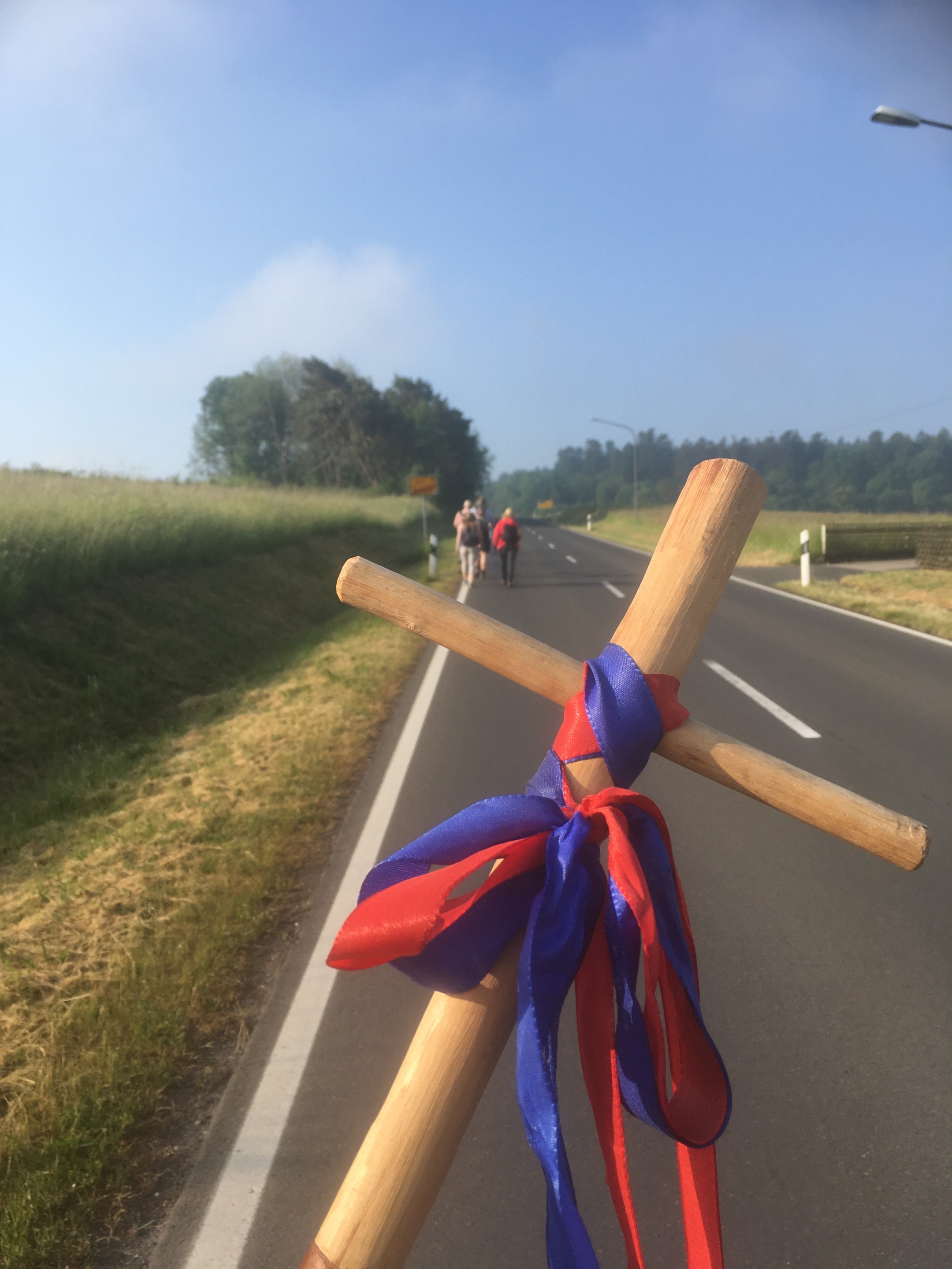 Pligerkreuz aus Holz mit blau-roter Schleife im Hintergrund ist eine Straße.