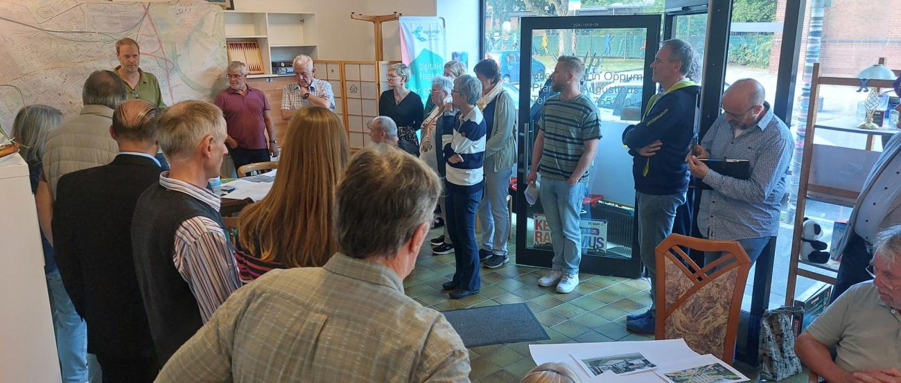 Zukunftsforum_MIO_September 26 (c) Dietmar Giesen Gruppe von Menschen in einem Raum mit großen Fenstern, einige stehen, andere sitzen an einem Tisch mit ausgebreiteten Papieren.